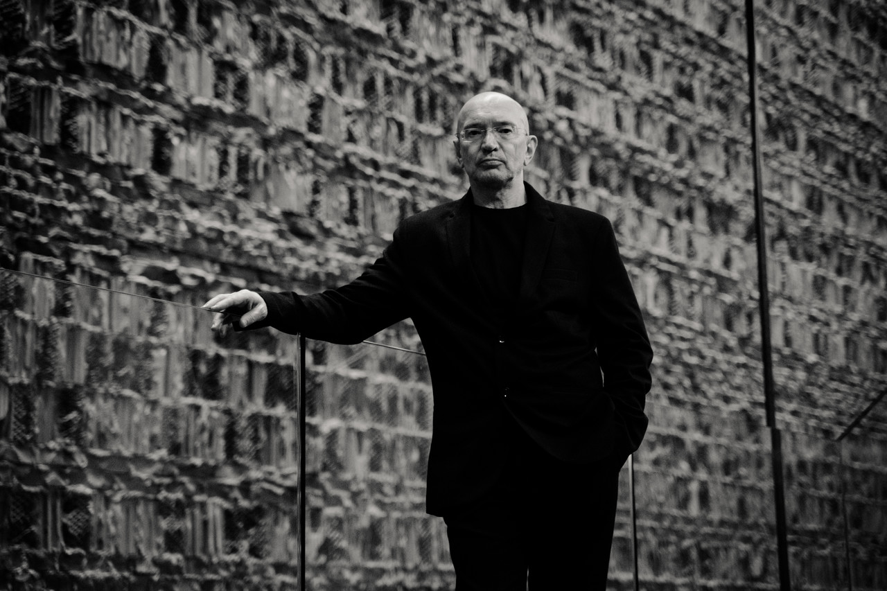 prof. Bogusław Stelmach. Zdjęcie monochromatyczne, mężczyzna w średnim wieku ubrany na czarno stoi oparty o mur.