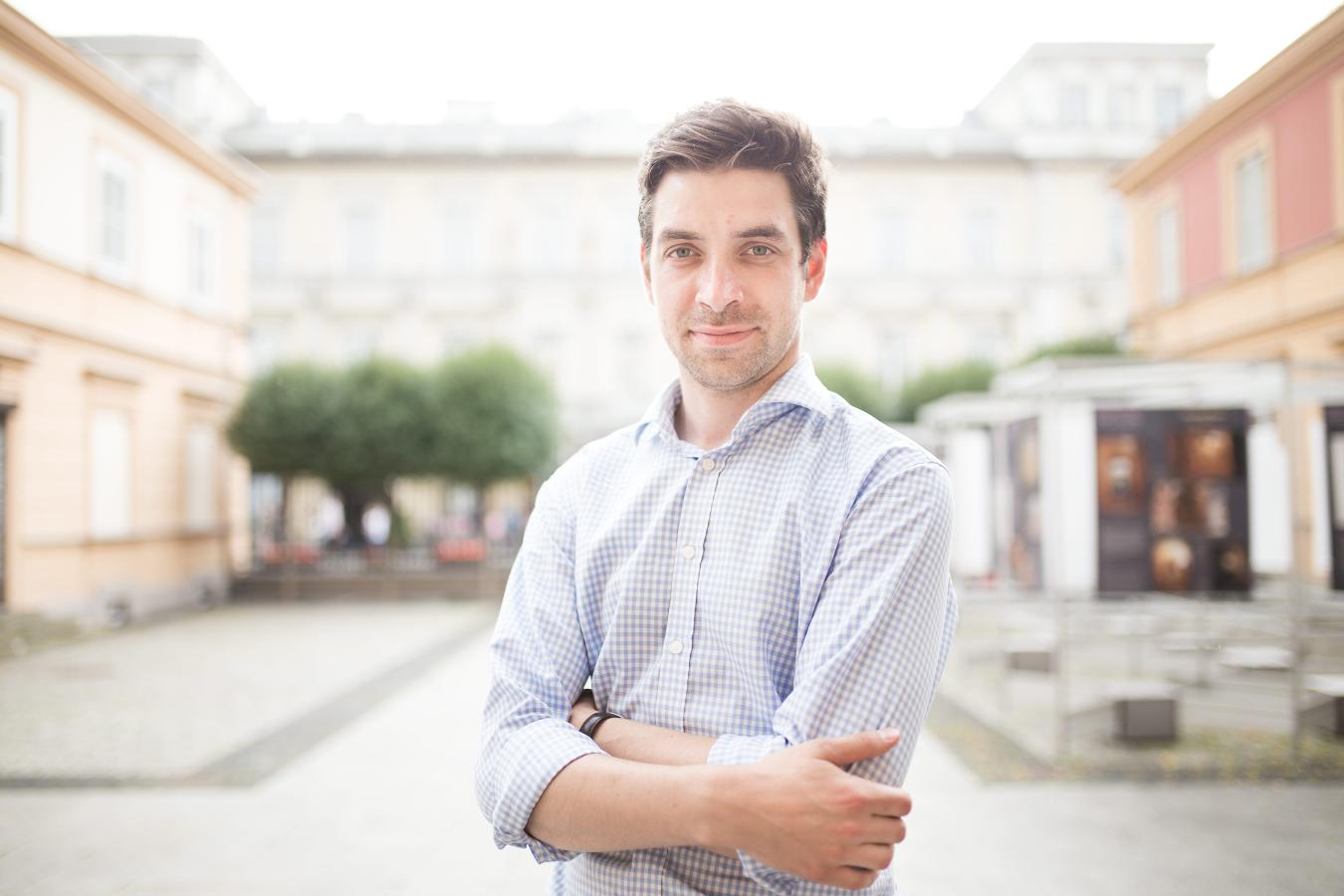 Michał Krasucki Stołeczny Konserwator Zabytków. Mężczyzna w średnim wieku w błękitnej koszuli stoi na tle budynku. W tle drzewa.