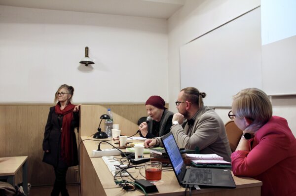 Debata Nazwy Warszawy. Eksperci debaty siedzący za biurkiem i dyrektorka CBKW prowadząca debatę.